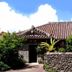 Minshuku Rakutenya in Ishigaki with a tiled roof, stone wall, and lush greenery under a blue sky