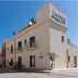 Pharos in San Vito Lo Capo on a sunny street corner with balconies and rooftop flags