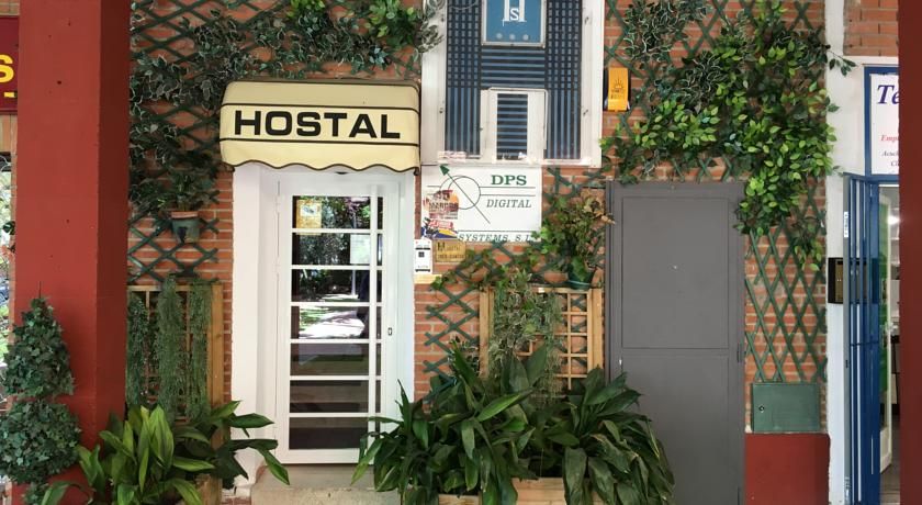 Hostal Tres Cantos entrance in Tres Cantos with hostal sign, white door and leafy potted plants