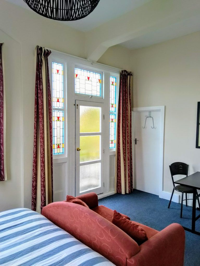 Crashpalace Napier room with stained-glass door, striped sofa, and small table by the window