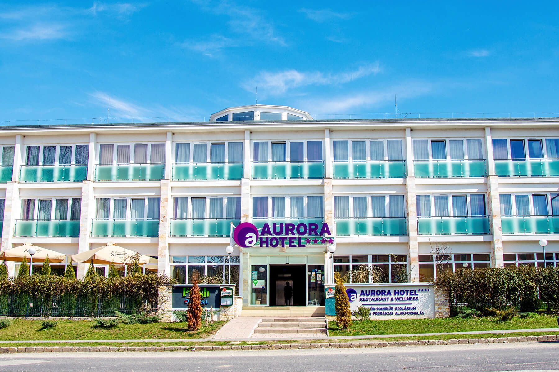 Hotel Aurora in Miskolc, exterior with glass balconies and a central entrance beneath a blue sky