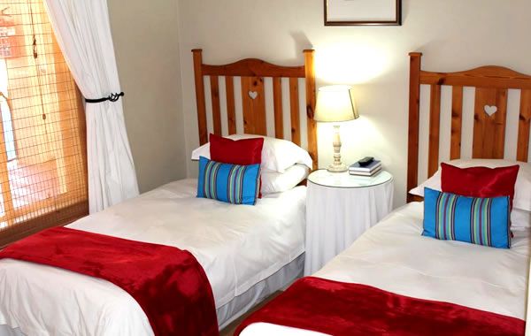 Blommenberg Guest House in Clanwilliam, twin bedroom with wooden headboards, bedside lamp and red throws.
