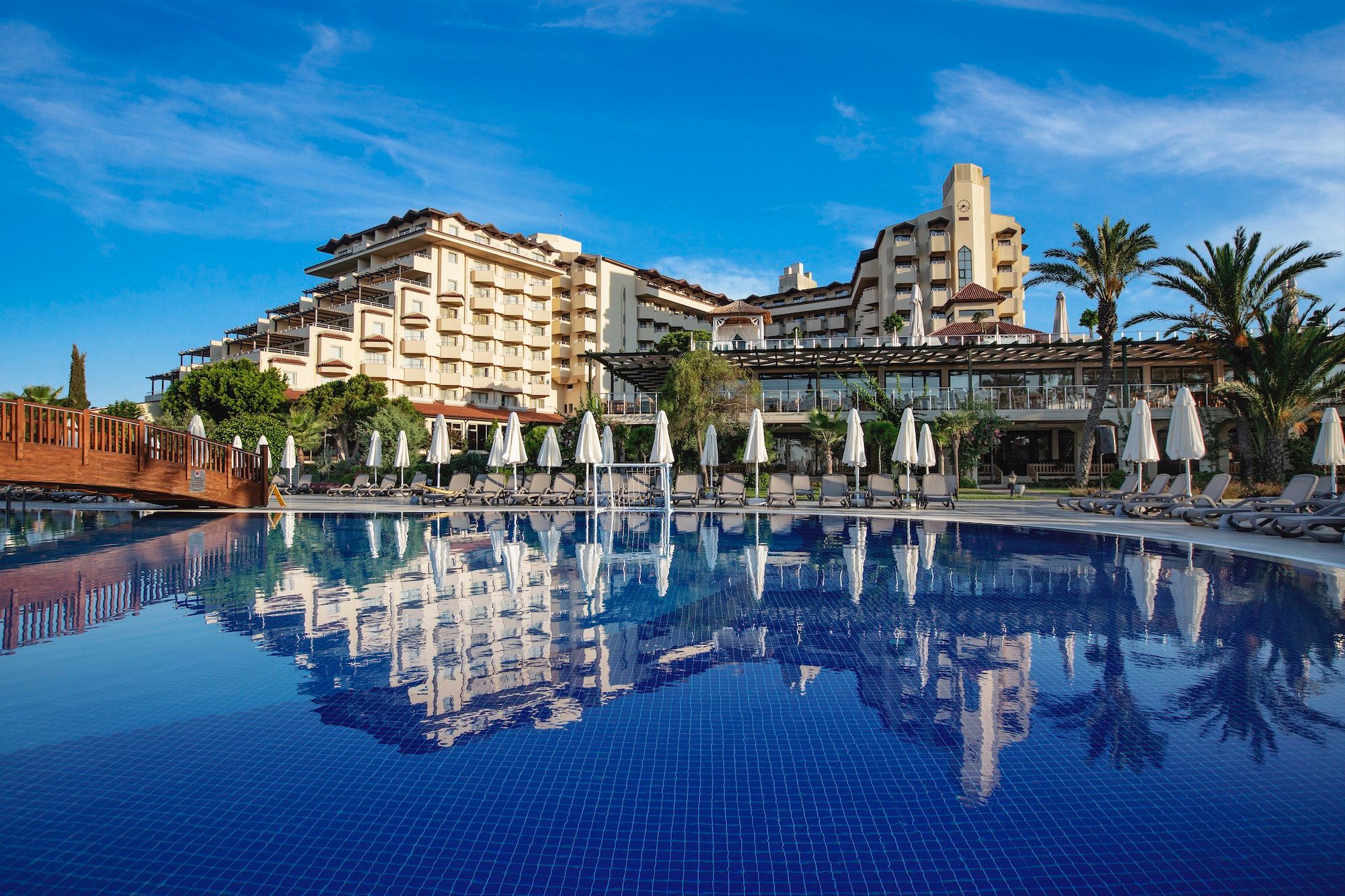 Bellis Deluxe Hotel in Belek with a large outdoor pool reflecting the hotel and palm trees