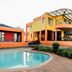 Grand View B&B in Johannesburg with a curved pool, patio seating and colorful guesthouse exterior