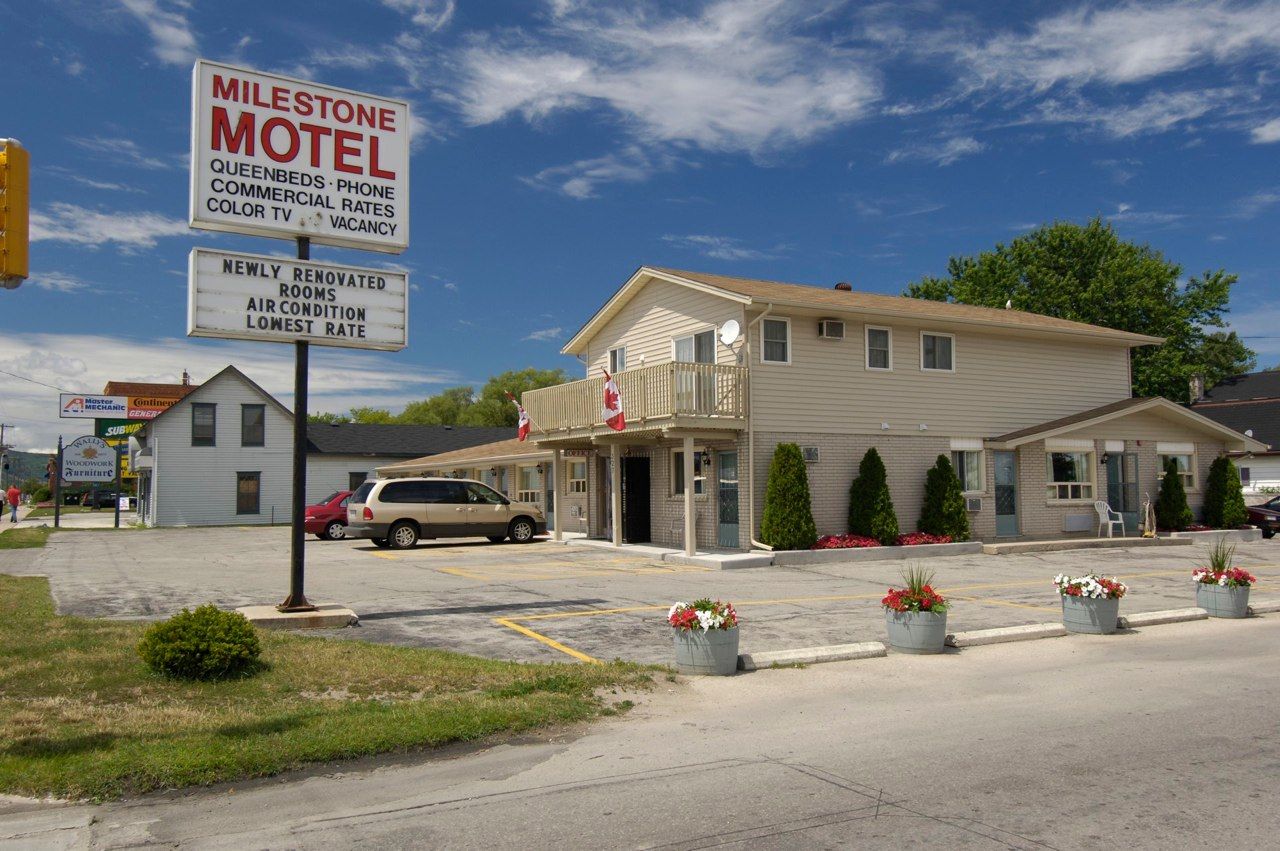 Milestone Motel in Collingwood with roadside sign, parking lot, and two-story exterior under blue sky
