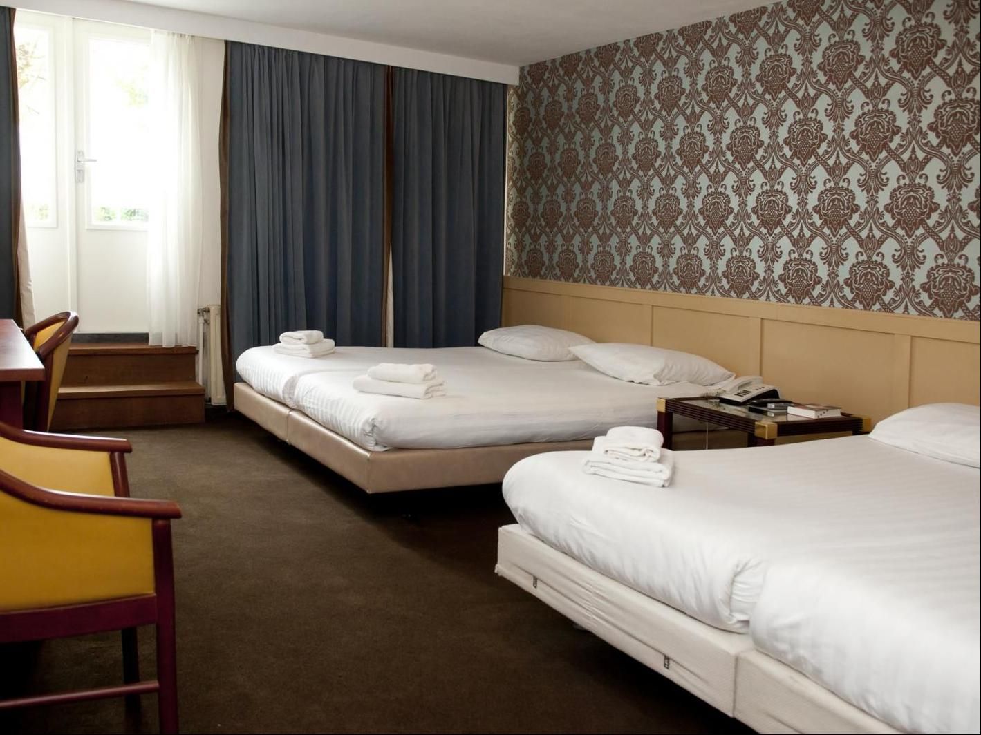 Hotel 74 Amsterdam room with two beds, patterned wallpaper, and window with curtains