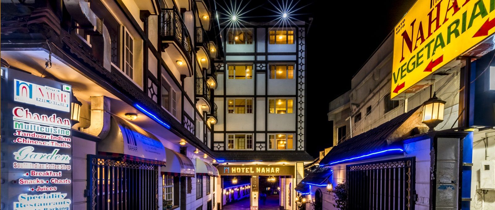 Hotel Nahar Nilgiris in Ooty at night, with lit facade and narrow street between buildings