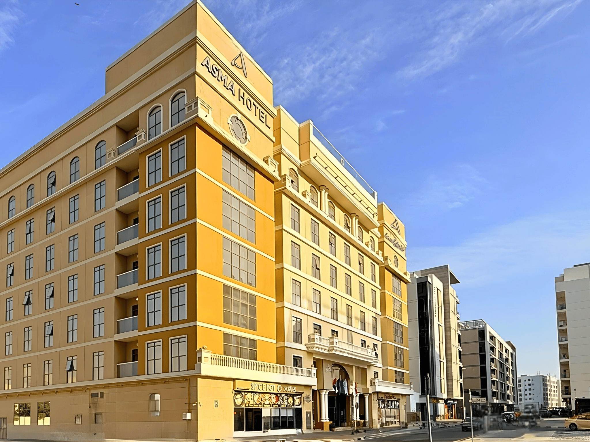 Asma Hotel Dubai exterior on a sunny street, featuring a yellow facade and arched entrance