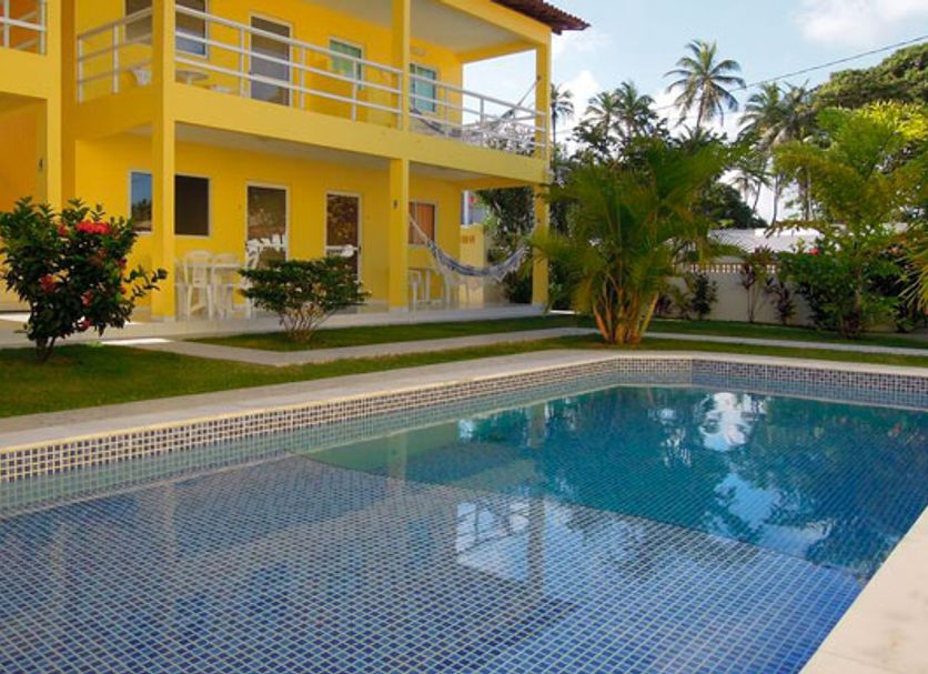 Pousada Joia Rara in Porto de Galinhas with a pool beside a bright yellow two-story building