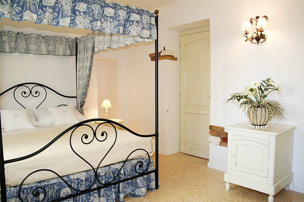 Ca' Ottocento in Lazise: wrought-iron four-poster bed, wall sconce, and white cabinet in a cozy room