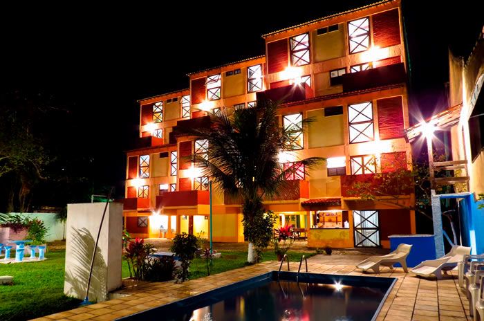 Apart Hotel Marinas Da Lagoa in Saquarema with lit pool, palm trees, and illuminated exterior at night