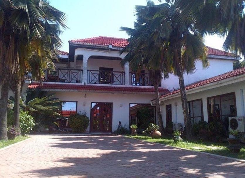 La Paradise Inn in Accra with a two-story white building, red roof, and palm-lined driveway
