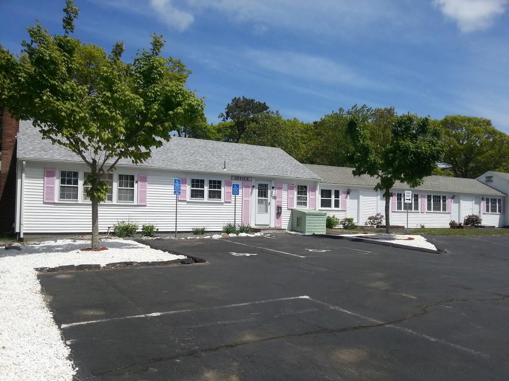 Bass River Motel in South Yarmouth, white motel exterior with pink shutters and a paved parking lot