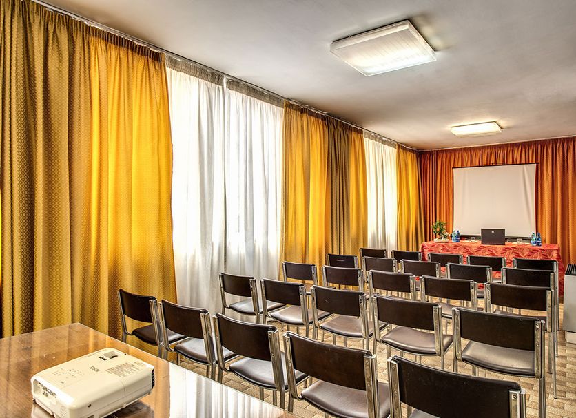Hotel Santa Maura in Rome meeting room with rows of chairs, projector screen and orange drapes
