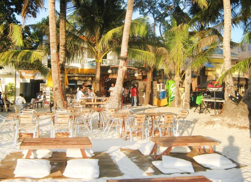 White Beach de Boracay beachside dining area with wooden tables, chairs, and palm trees in Boracay