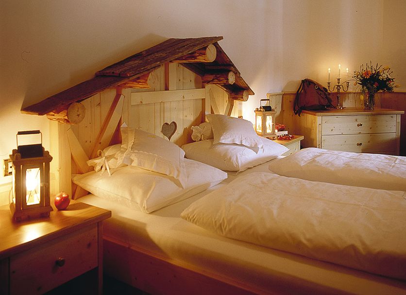 Alpenhotel Plaza in Santa Cristina Valgardena: cozy alpine bedroom with carved wood headboard and lanterns