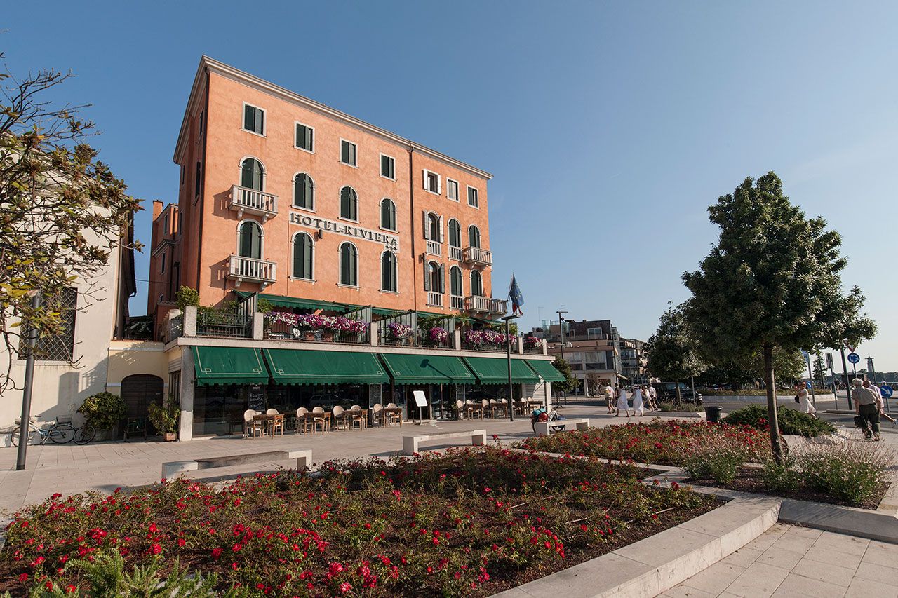 Hotel Riviera in Venice with a peach façade, green awnings, balconies and a flower-lined terrace