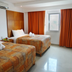 Suites Gaby Cancun in Cancún: twin beds, orange curtains, wall AC and window in a simple guest room.