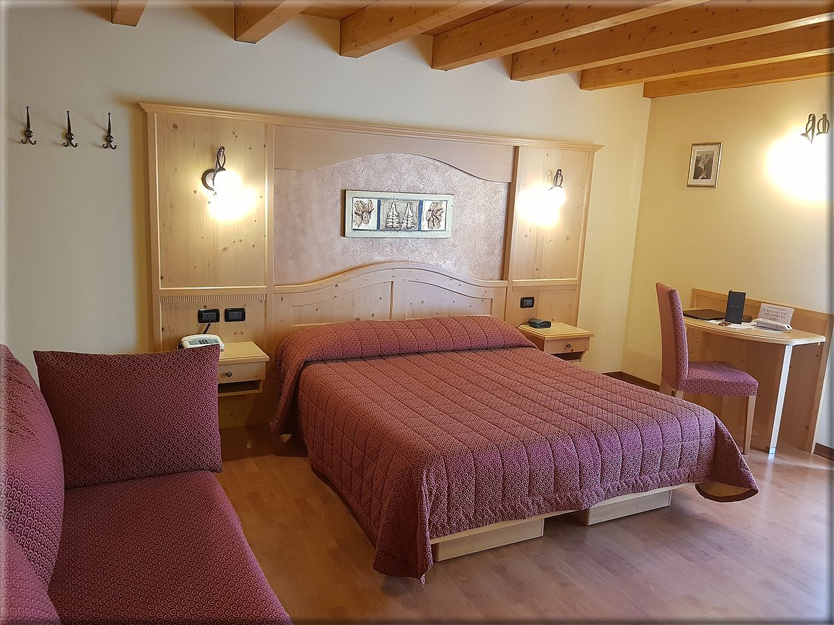 B&B La Montanara room in San Martino di Castrozza with double bed, sofa, and wooden beam ceiling