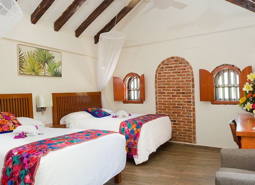 Hotel La Joya Isla Mujeres room with two beds, exposed beams, and brick arch window in Isla Mujeres
