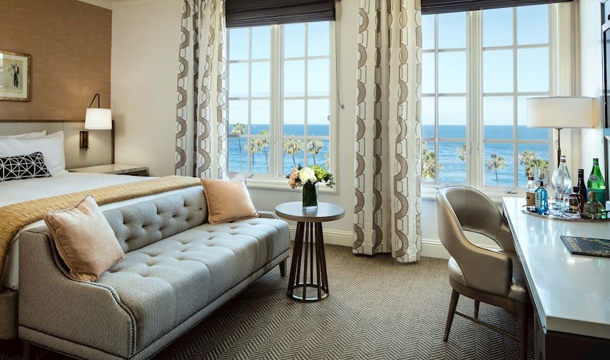 La Valencia Hotel in San Diego guest room with ocean view, tufted sofa, desk, and large windows