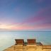 Argyro Rent Rooms in Kritsa with two lounge chairs on a deck overlooking calm sea at sunset