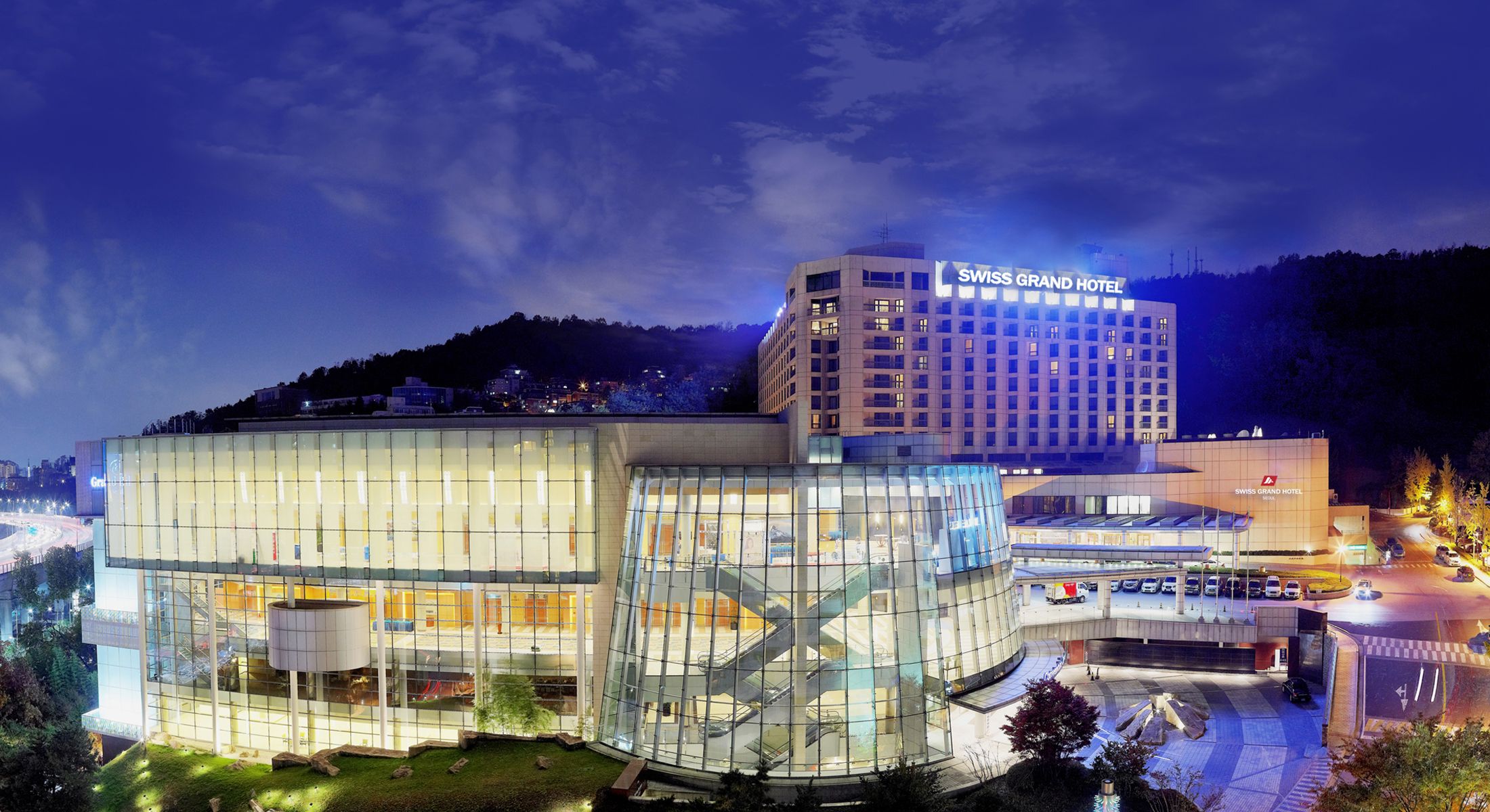 Swiss Grand Hotel in Seoul with illuminated glass facade and mountain backdrop at night