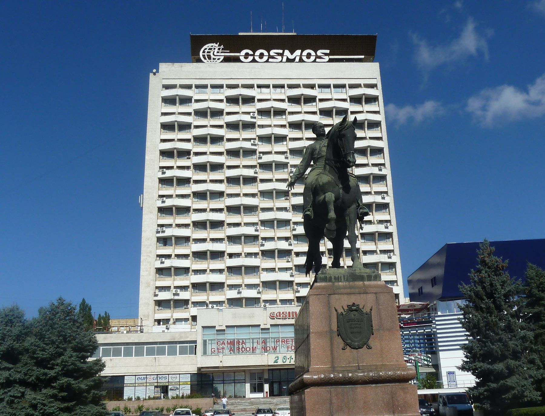 Hotel Cosmos in Chisinau with a tall facade behind an equestrian statue under a blue sky