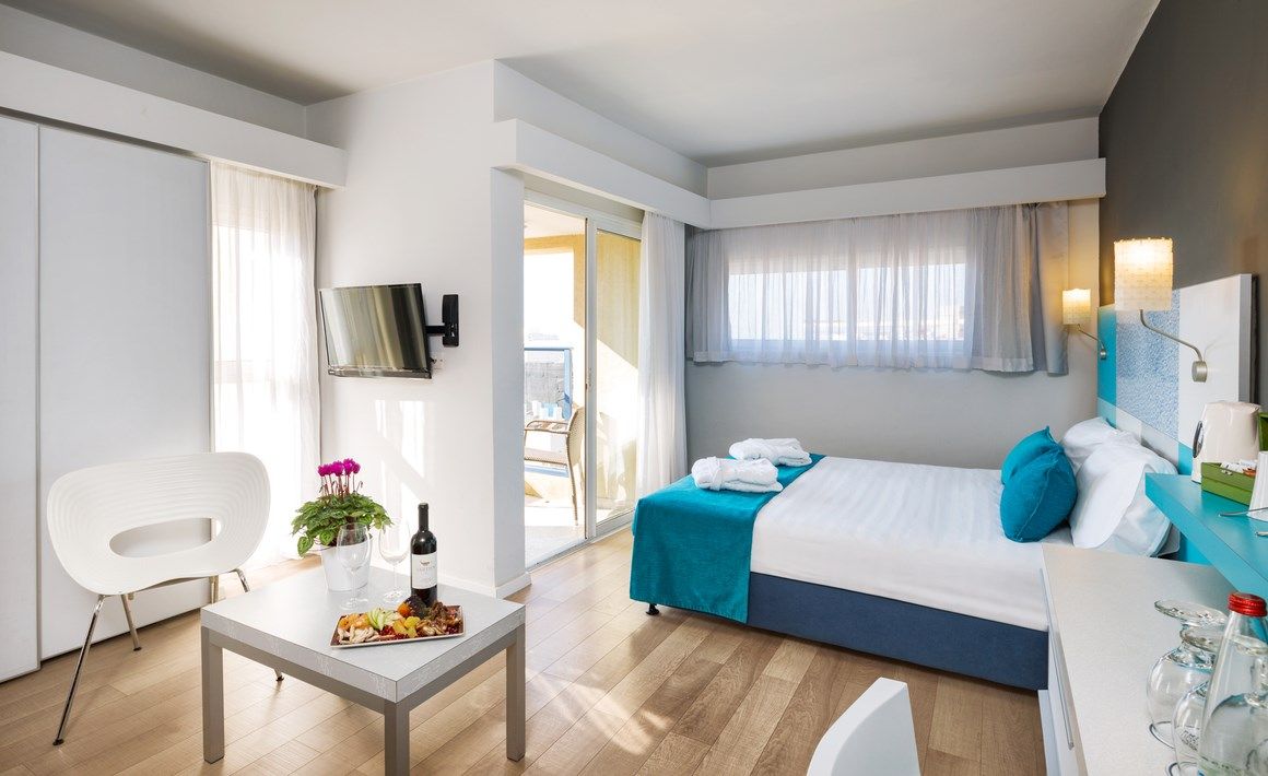 Prima City Hotel Tel Aviv room with bed, sofa, wall-mounted TV and balcony view