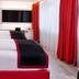Dormero Hotel Dresden City room with three white beds, red accents, TV and floor-to-ceiling curtains in Dresden