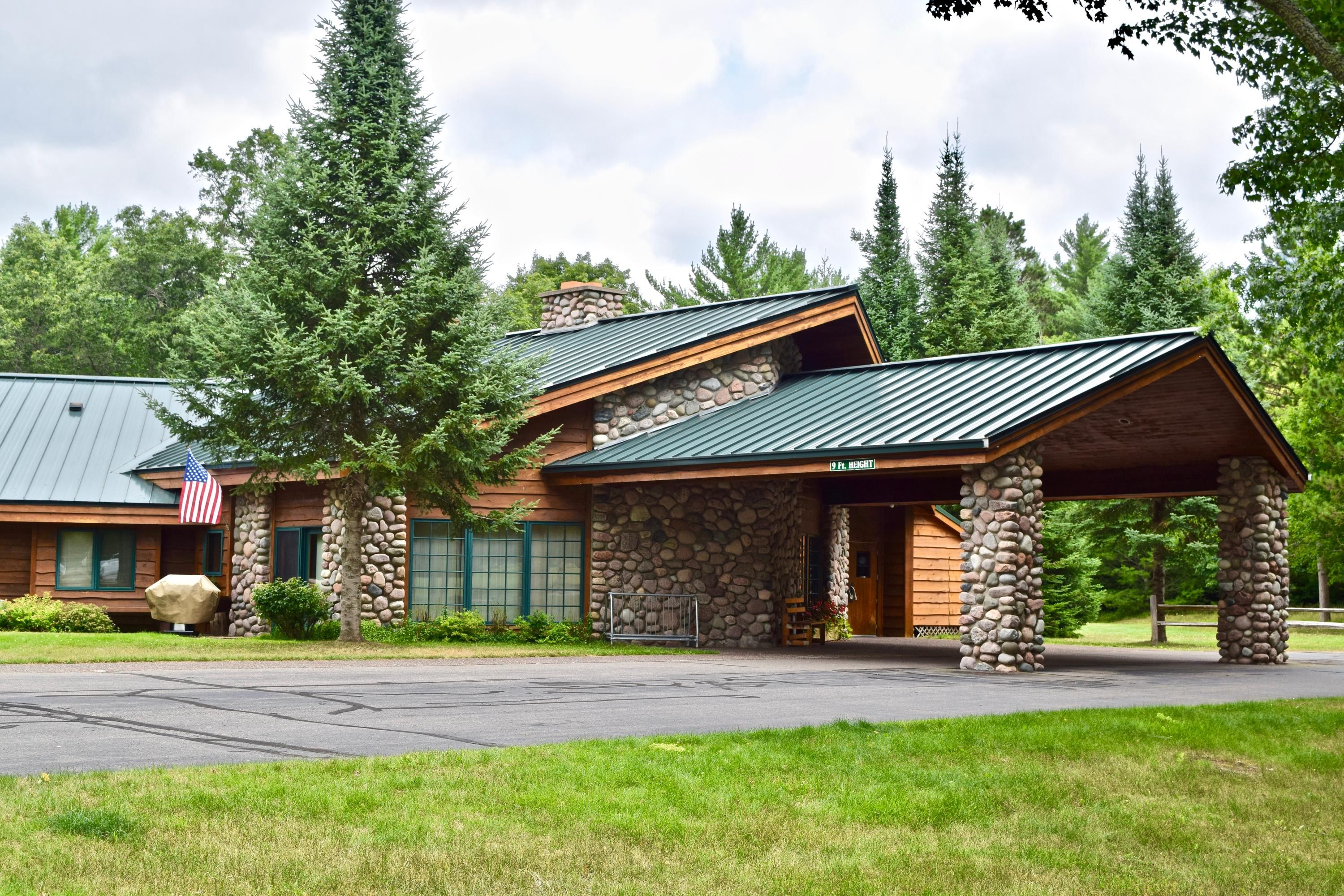 Whitetail Lodge in Saint Germain with stone lodge entrance, covered driveway, and pine trees