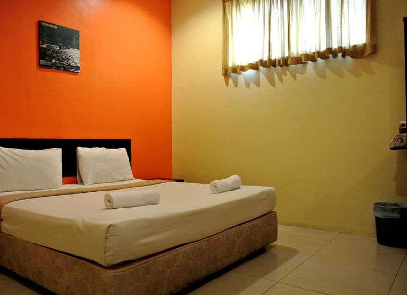 Wau Hotel & Cafe in Jerantut room with double bed, orange accent wall and curtained window