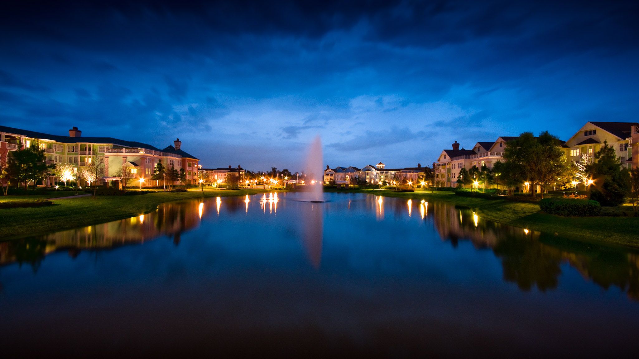 Disney's Saratoga Springs Resort & Spa in Lake Buena Vista with a lit fountain reflecting on a calm lake at dusk