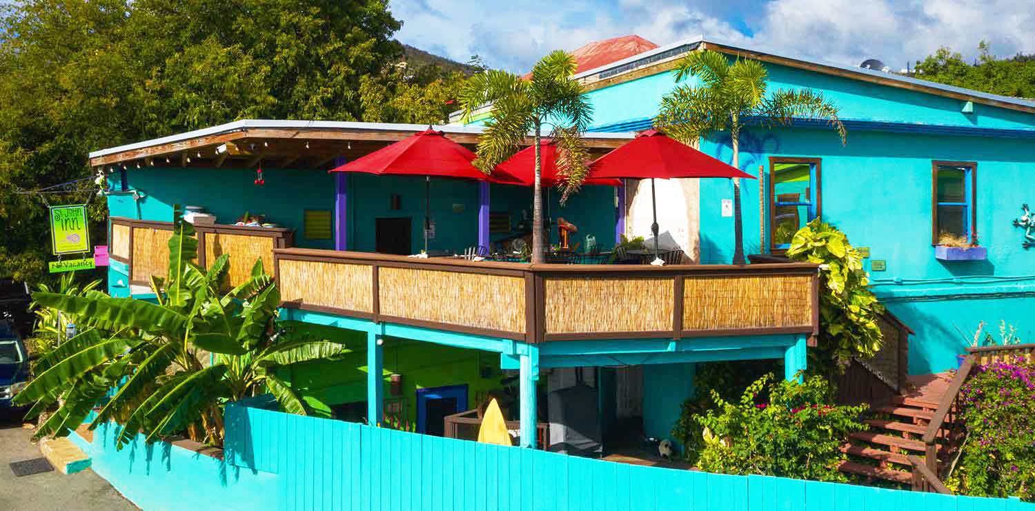 St John Inn in St. John with turquoise exterior, balcony, red umbrellas and tropical greenery