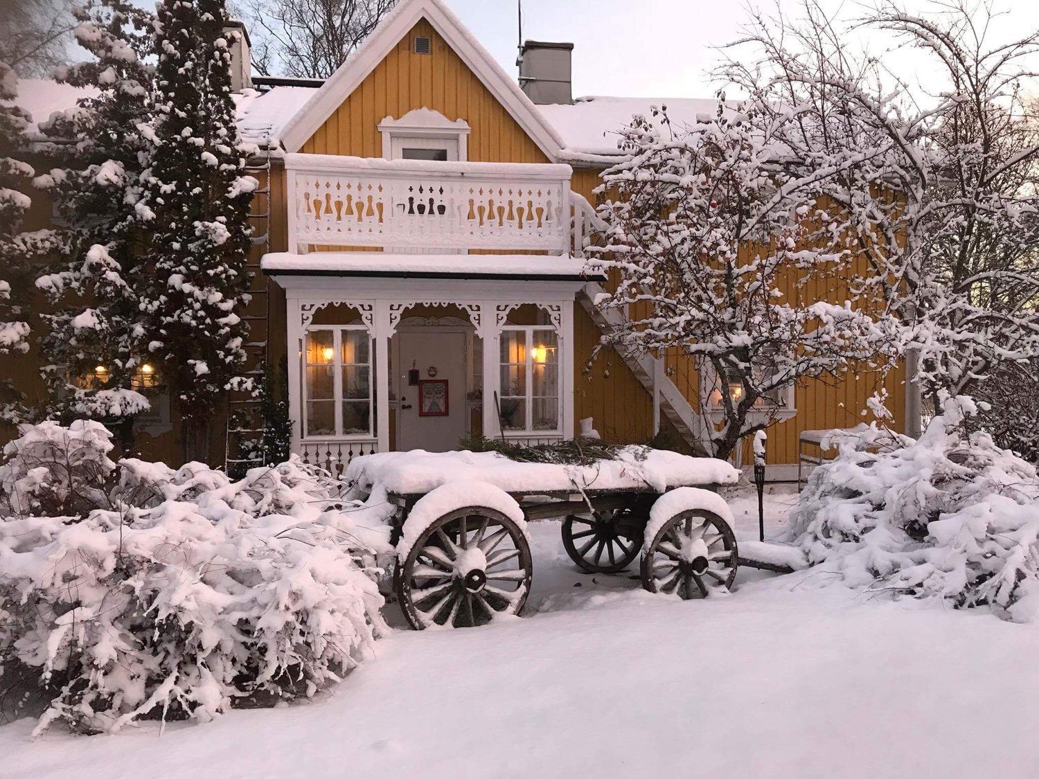 Vardshuset Idyllen in Söråker, snow-covered yellow house with balcony and rustic wagon in front