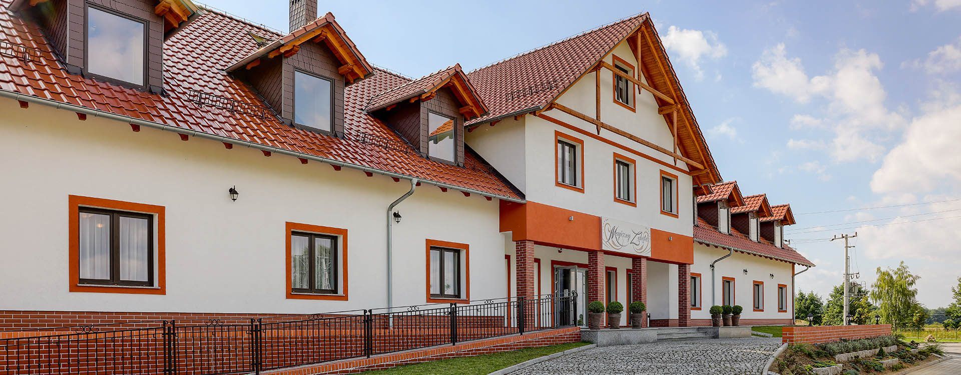 Hotel Magiczny Zakatek in Kędzierzyn-Koźle, exterior of a multi-gabled hotel with red roof and brick walkway