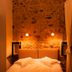 Guesthouse Theonimfi in Dimitsana: cozy stone-walled bedroom with warm bedside lighting and canopy curtain