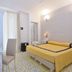 Hotel7Bello in Minori: bright guest room with yellow bedspread, desk, chair, wall sconces and window