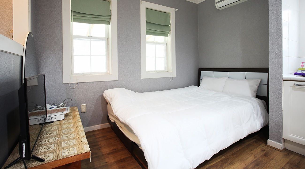 Yesolnuri Pension in Yeongwol bedroom with white bed, two windows, wood floor and TV