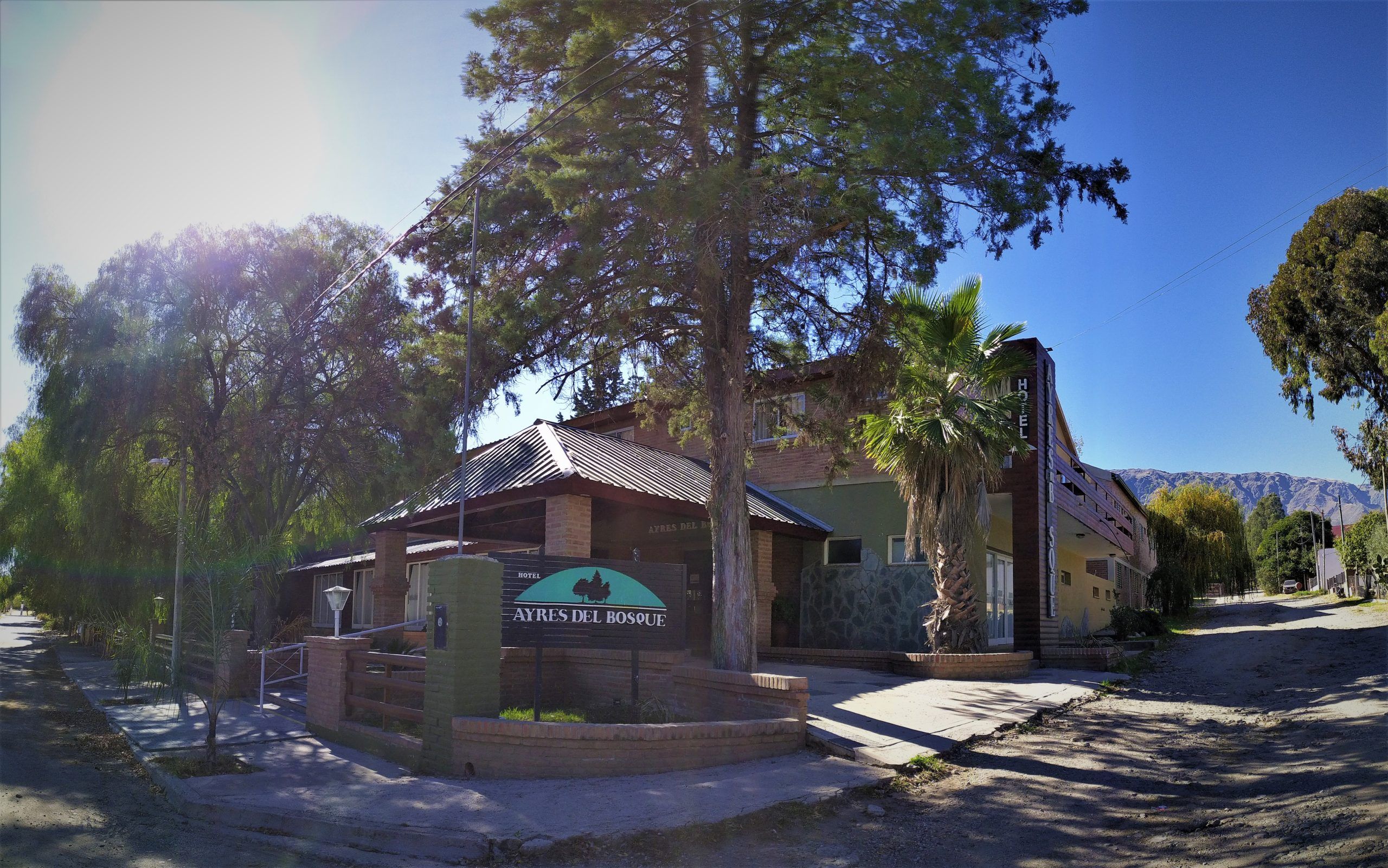 Ayres Del Bosque in Villa de Merlo, roadside hotel entrance with trees and mountain backdrop
