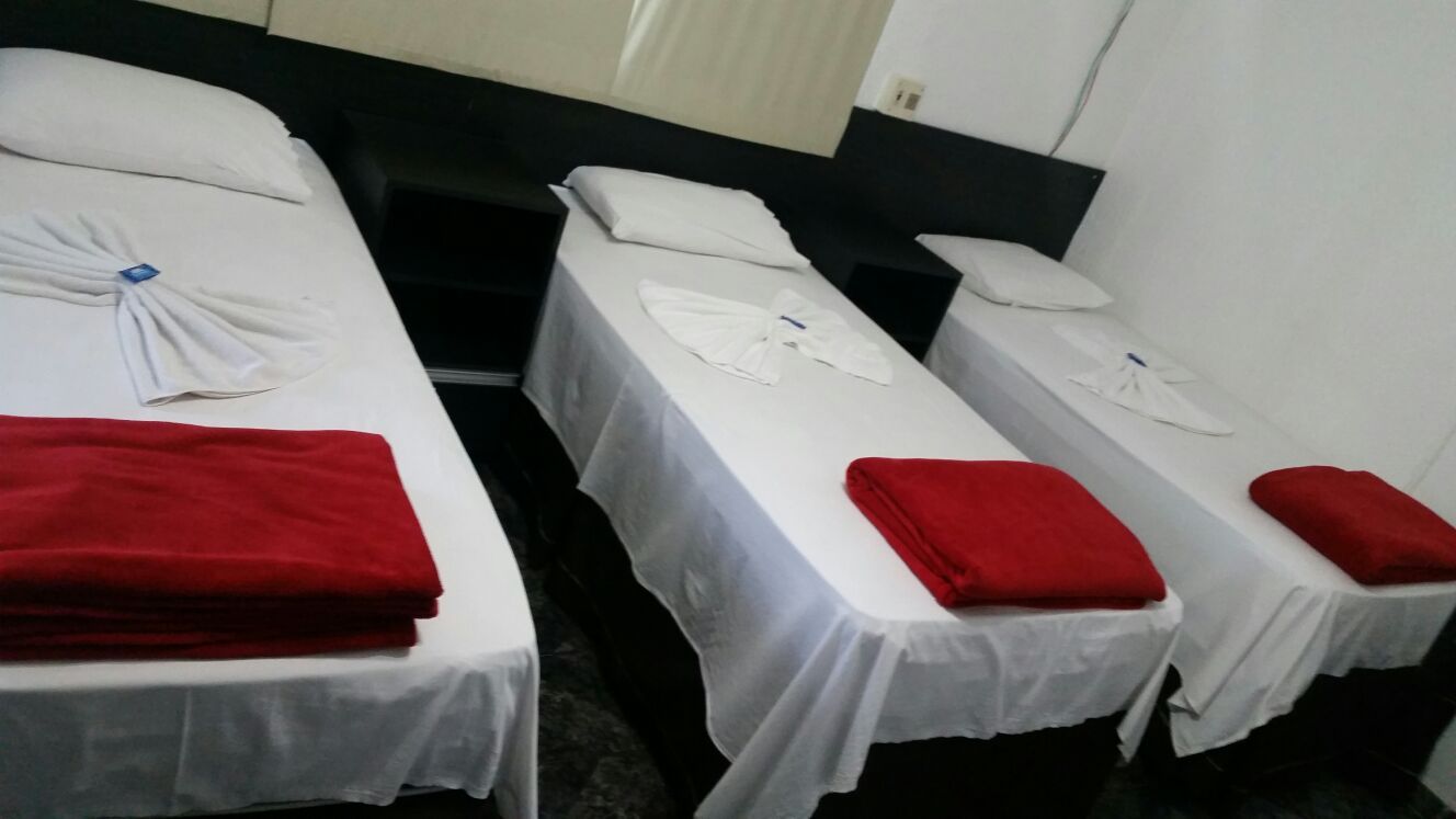 Hotel Anápolis in Anápolis: three single beds with white linens and red towels in a simple room