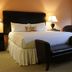 The Clarke in Waukesha: warmly lit guest room with king bed, two lamps, bench, and window seat.
