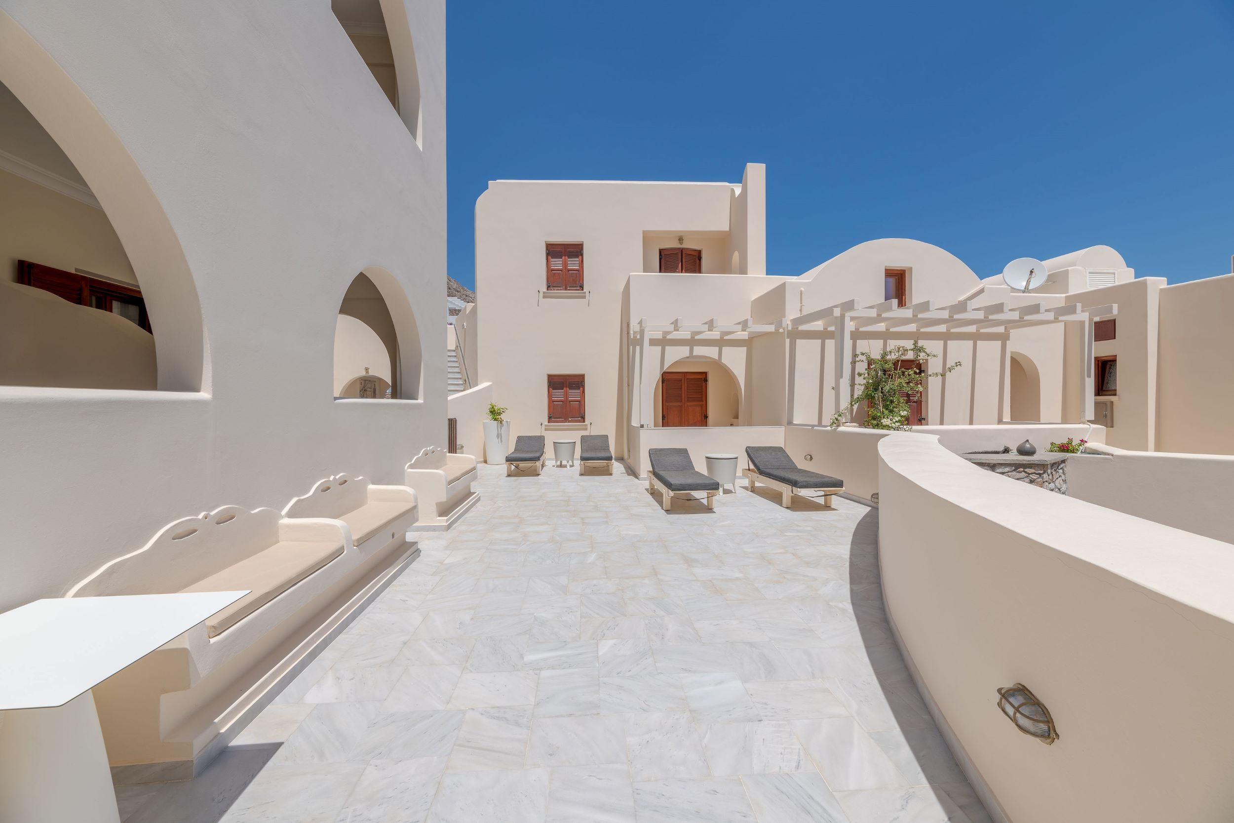 Epavlis Hotel & Spa in Kamari: sunlit rooftop terrace with lounge chairs and white Cycladic architecture