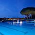 Garden Toscana Resort in San Vincenzo: illuminated outdoor pool at dusk with blue water and lounge area
