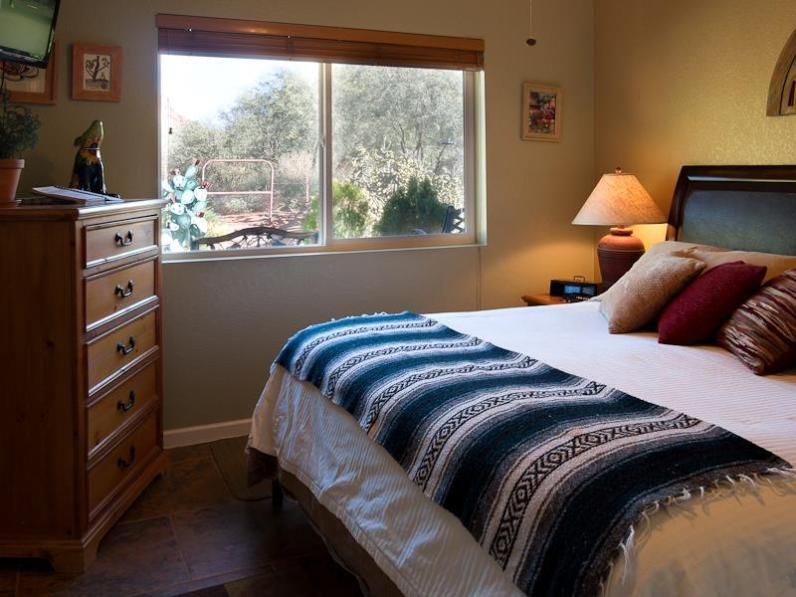 Cozy Cactus Sedona guest room with bed, dresser and large window overlooking desert greenery