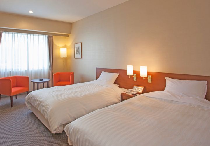 Mutsu Grand Hotel in Mutsu guest room with two twin beds, orange chairs, and window light
