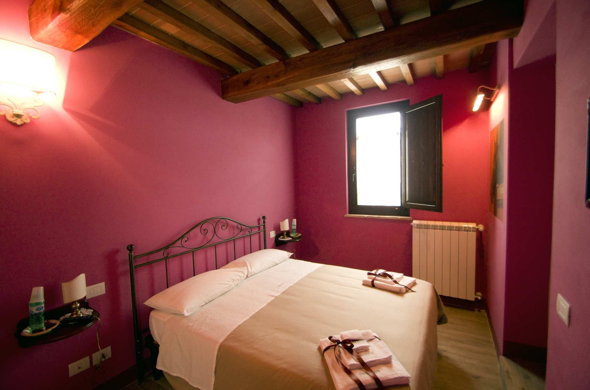 Diana House in Ripa guest room with magenta walls, double bed, and wood-beam ceiling
