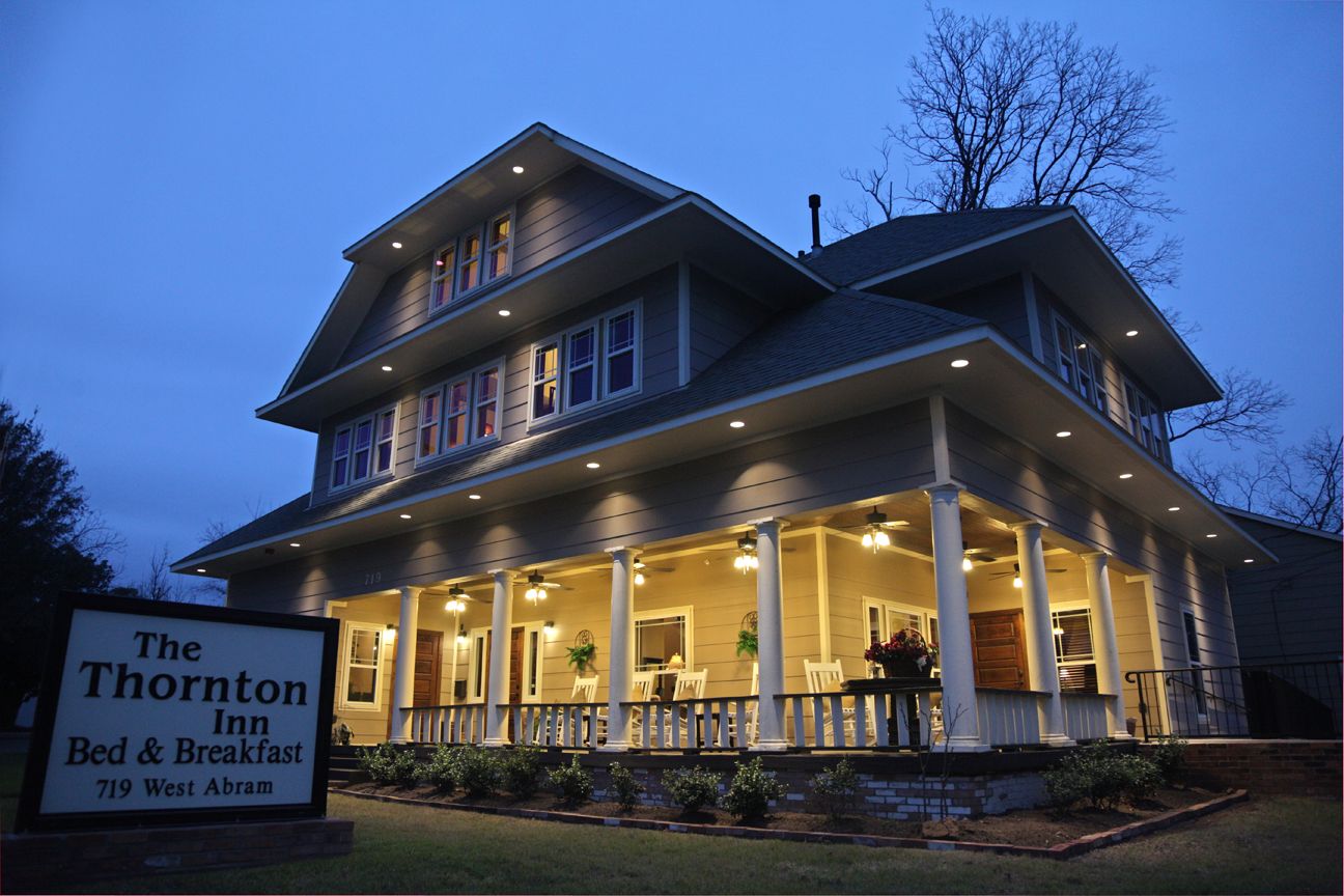 The Thornton Inn Bed and Breakfast in Arlington at dusk, showing a wraparound porch and lit exterior