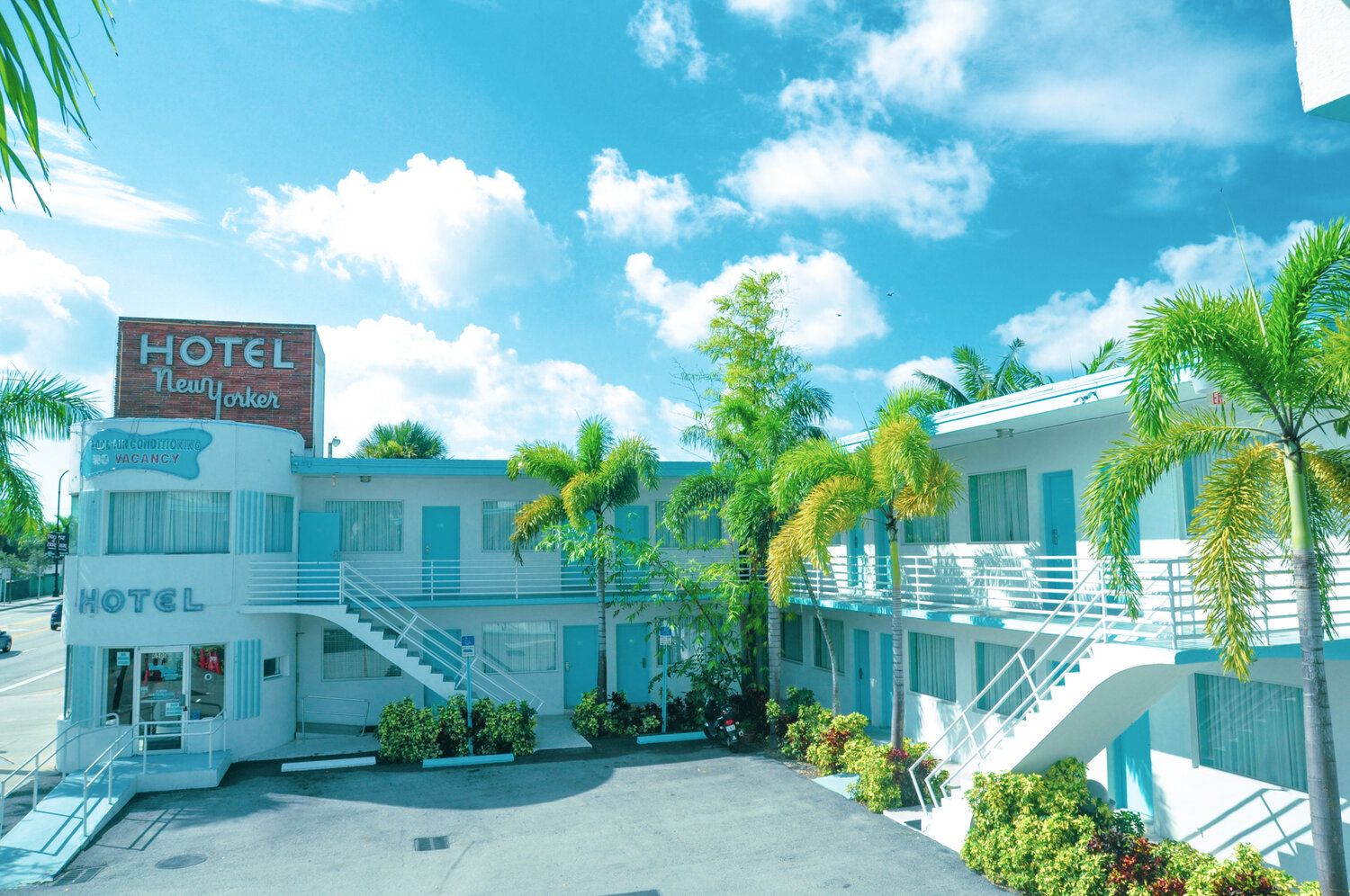 The New Yorker Hotel Miami exterior with palm trees, bright blue sky, and two-story motel-style rooms in Miami