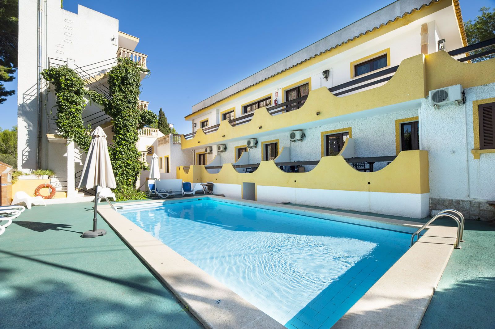 Don Carlos in Peguera with a sunny outdoor pool beside a yellow-and-blue hotel building